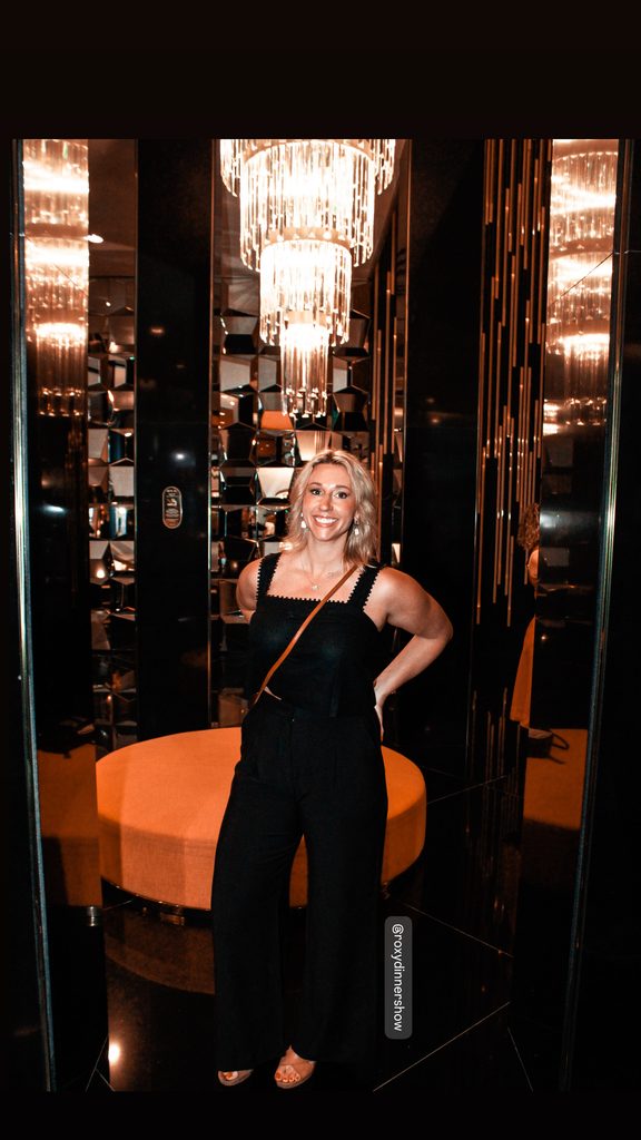 Amanda Dante at Roxy Dinner Show in Rio de Janeiro, standing beneath a chandelier surrounded by mirrored walls.