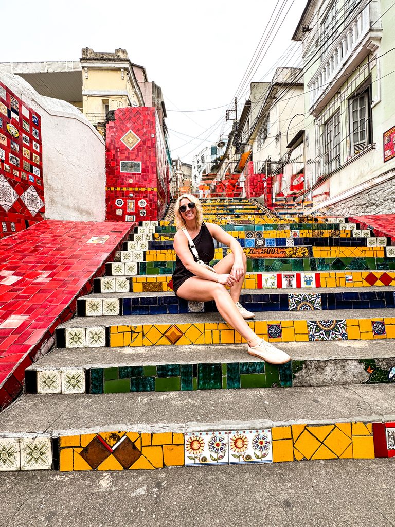 Amanda Dante sitting on the colorful mosaic-tiled Selarón Steps in Rio de Janeiro, Brazil.