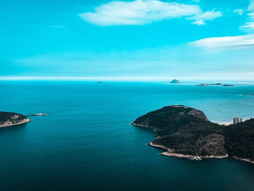 Atlantic Ocean and offshore islands viewed from Sugarloaf Mountain in Rio de Janeiro, with forested headlands in the foreground.