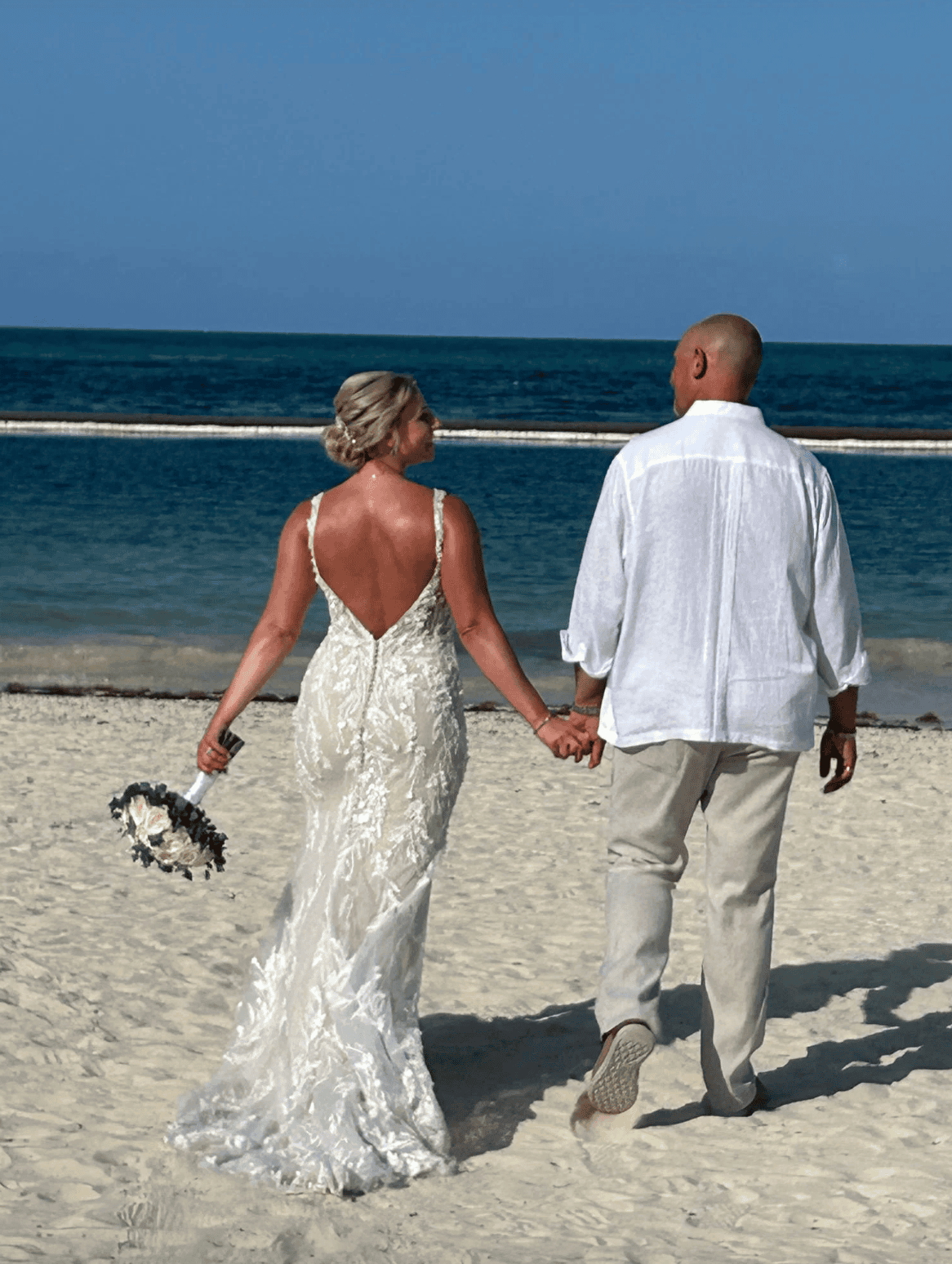 Bride and groom walking hand in hand on a Caribbean beach after their destination wedding ceremony.