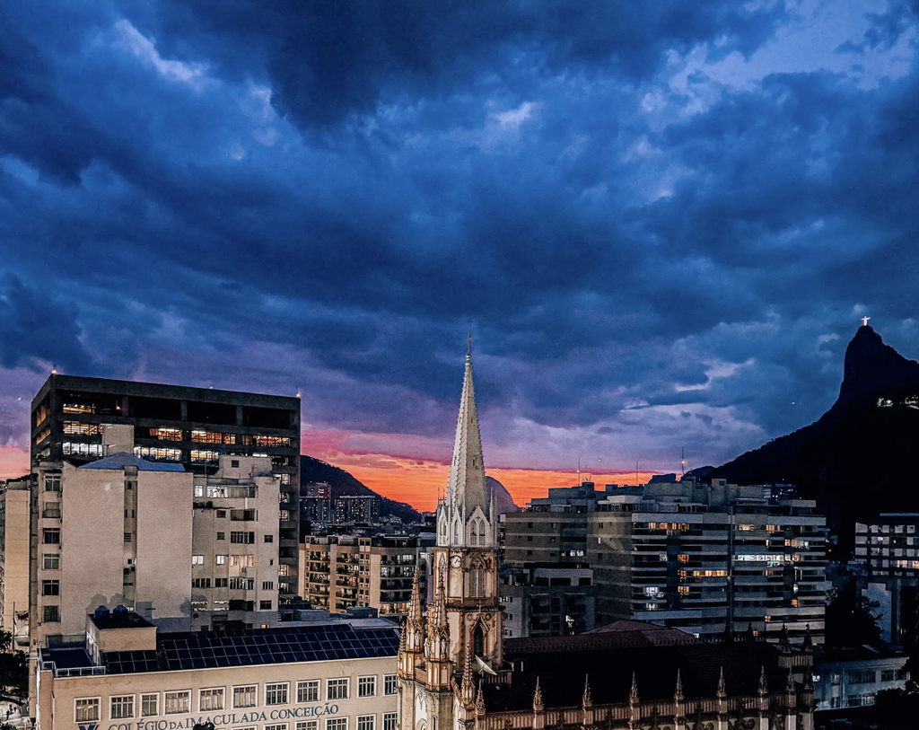 Sunset over Botafogo in Rio de Janeiro, with a church spire in the foreground and Christ the Redeemer on Corcovado in the distance.