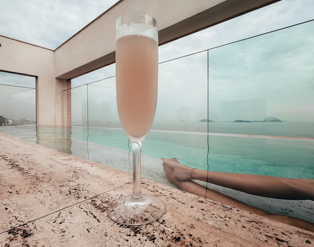 Pink cocktail beside the rooftop pool at JANEIRO Hotel in Rio de Janeiro, overlooking the ocean and offshore islands.
