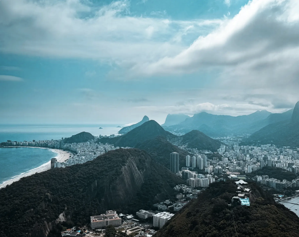 View from Sugarloaf Mountain over Copacabana Beach, Rio de Janeiro’s skyline, and forested mountains, with a cable car in the foreground.