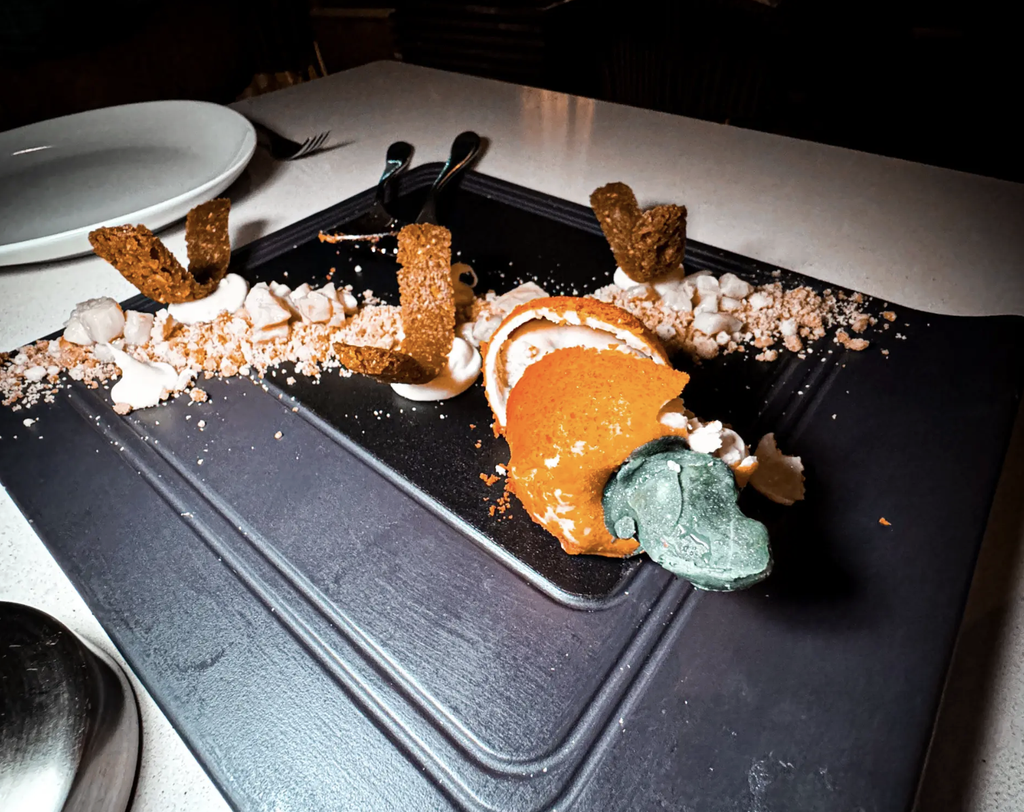 Cashew-shaped dessert with orange and green details, cream, and crisp garnishes on a black plate in Rio de Janeiro.