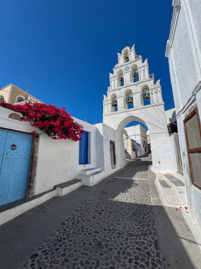 Traditional whitewashed church and cobblestone street with blue doors and bougainvillea in Santorini, Greece