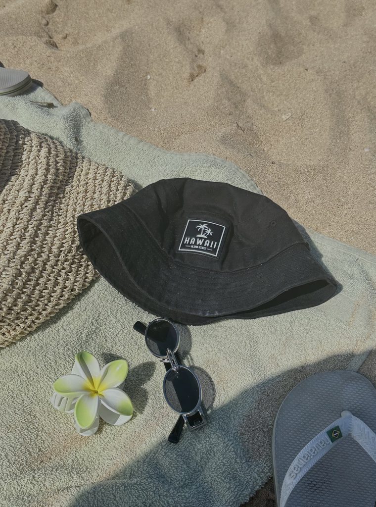 Hawaii beach essentials with a sun hat, sunglasses, and plumeria flower on the sand